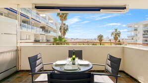 A balcony with a round table set for two, overlooking a beach and palm trees. - Charming Apartment With Patio (Roses)