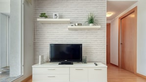 A modern living room with a white brick wall, a flat-screen TV on a white cabinet, and a wooden door in the background. - Charming Apartment With Patio (Roses)