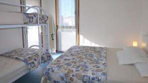 A room with bunk beds and a single bed, a window with curtains, and a wall-mounted light. - Apartment Porto Santa Margherita by Beach (Caorle)