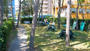 A pathway lined with trees leading to a grassy area with outdoor furniture. - Apartment Porto Santa Margherita by Beach (Caorle)