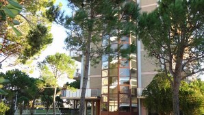 A modern building with a glass facade, surrounded by trees and a well-maintained lawn. - Apartment Porto Santa Margherita by Beach (Caorle)