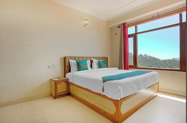 A bedroom with a wooden bed, white bedding, and a view of a green landscape through a large window.