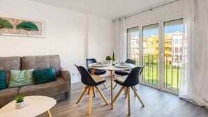 Una sala de estar moderna con un sofá, una mesa de comedor y sillas. Se ve un ventanal con vistas a edificios.