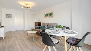 Una sala moderna con comedor. Incluye un sofá, una mesa de comedor con sillas, una mesita auxiliar y una lámpara del techo.