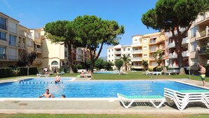 Una piscina rodeada de edificios de apartamentos, con árboles y sillas de descanso.