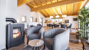 A modern living room with a wood-burning stove, grey sofas, a dining area, and a kitchen in the background. - Mountain-view Chalet in Wagrain (Wagrain)