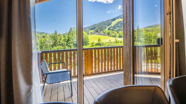 A balcony with a wooden railing, a chair, and a view of a green landscape with trees and a hill. - Mountain-view Chalet in Wagrain (Wagrain)