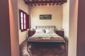 Un lit avec un cadre en métal, deux tables de chevet avec des lampes, une fenêtre avec des volets rouges et un tableau accroché au mur.