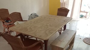 Un coin repas avec une table en bois et des chaises en osier, un banc et une chaise avec un coussin.