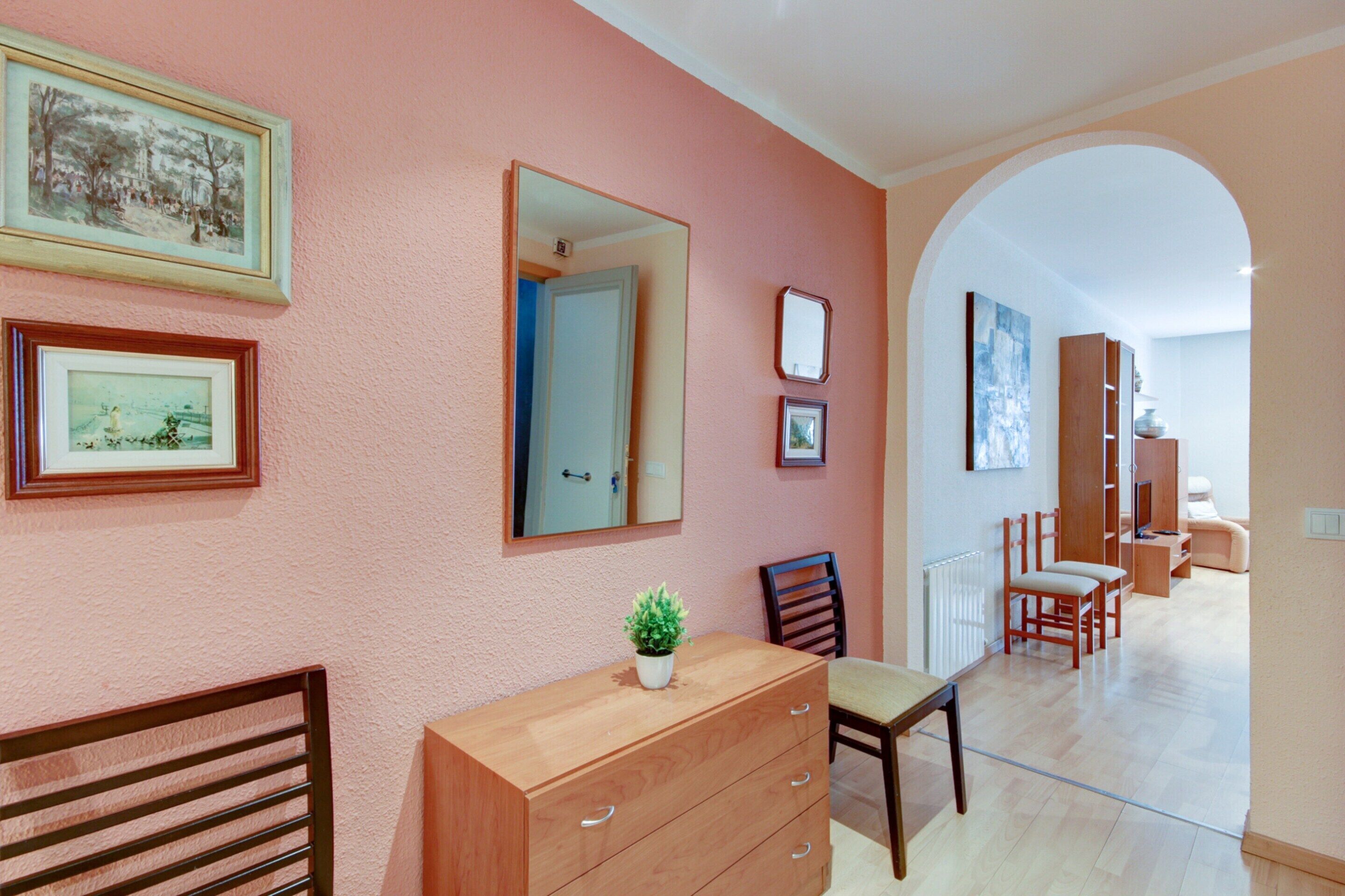 A room with a wooden dresser, a chair, a small potted plant, and framed pictures on the wall.
