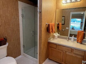 A bathroom with a glass shower enclosure, wooden vanity, and a large mirror.