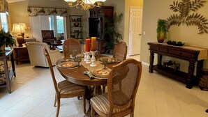 A dining area with a round table, chairs, and a chandelier. There is a door and a plant in the background.