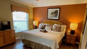 A bedroom with a large bed, two bedside lamps, a television on a dresser, and a window with blinds.