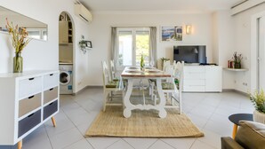 Una cocina moderna con armarios blancos, una mesa de comedor con sillas, lavadora y televisor.
