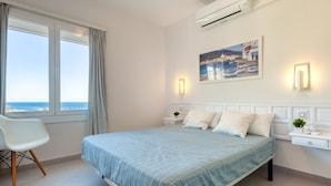 Un dormitorio con una cama, una silla, una mesita de noche, un aire acondicionado instalado en la pared y una ventana con cortinas.
