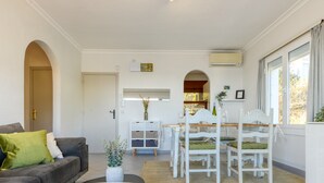 Una sala moderna con sofá, mesa de comedor y sillas. Se ve una puerta que da a otra habitación, un armario blanco y una ventana con cortinas.