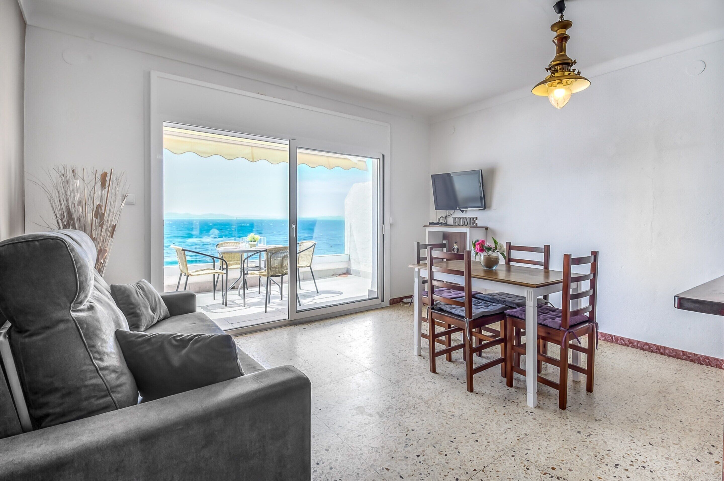 Un espace de vie comprenant un canapé, une table à manger avec des chaises, un téléviseur et une vue sur l’océan grâce à de grandes portes coulissantes.
