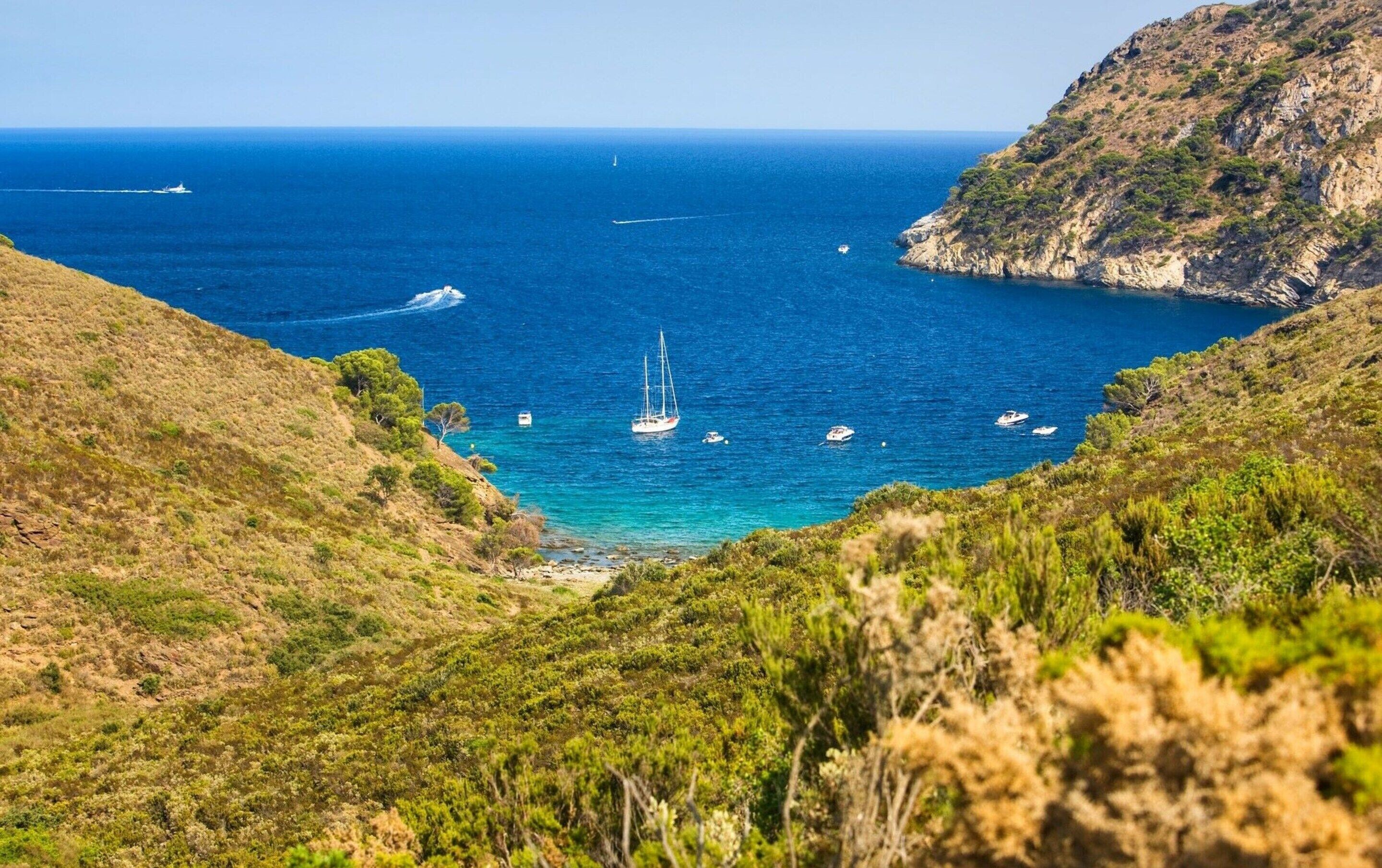 Un paysage côtier avec des bateaux sur l’eau, entouré de collines.