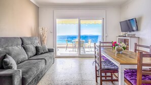 Ein Wohnzimmer mit grauem Sofa, einem Holzesstisch mit Stühlen und einem an der Wand befestigten Fernseher.