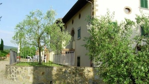 A stone wall, a grassy area, and a building with a tiled roof and arched windows. - Farmhouse in Poppi With Pool & Gardens (Poppi)