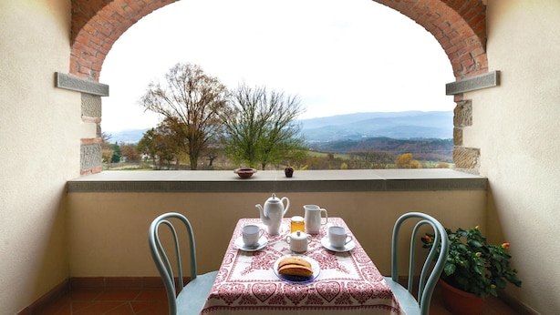 A balcony with a table set for tea, a view of the countryside, and a brick archway. - Farmhouse in Poppi With Pool & Gardens (Poppi)