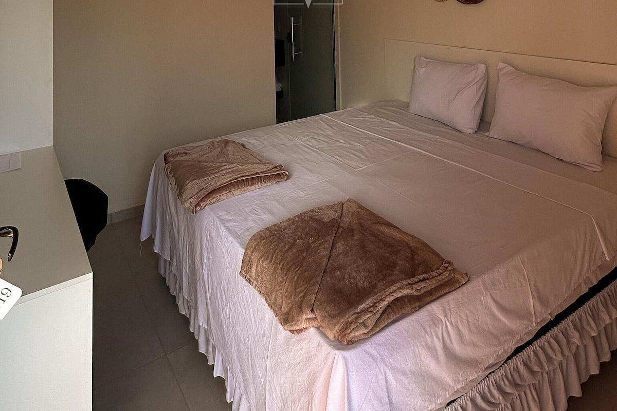 A bedroom with a bed, a desk, and an air conditioning unit.