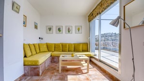 A living room with a yellow sofa, a wooden coffee table, and a large window with a view of buildings. - Apartment in Roses Near the Beach (Roses)
