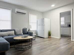 A modern living room with a grey sofa, a round coffee table, and a white refrigerator. - Riverside A6- EVV 1BR-1BA Apt (Evansville)