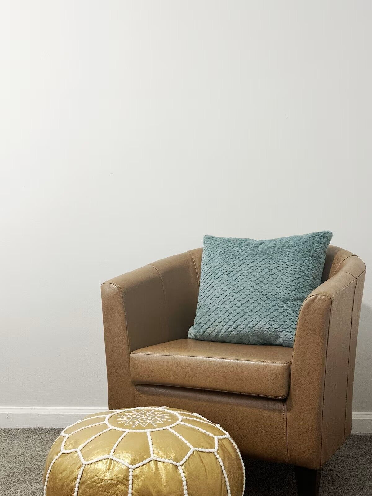 Un sillón de cuero color bronce con un cojín azul texturizado y un reposapiés con adornos dorados y blancos.