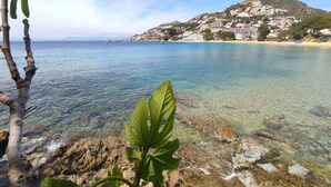 A coastal view with clear water, rocky shore, and a hillside with buildings. - Apartment in Roses Near Sandy Beach (Roses)