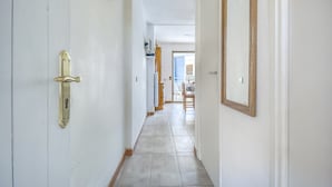 Um corredor com uma porta à esquerda, um espelho à direita e uma sala de jantar ao fundo.
