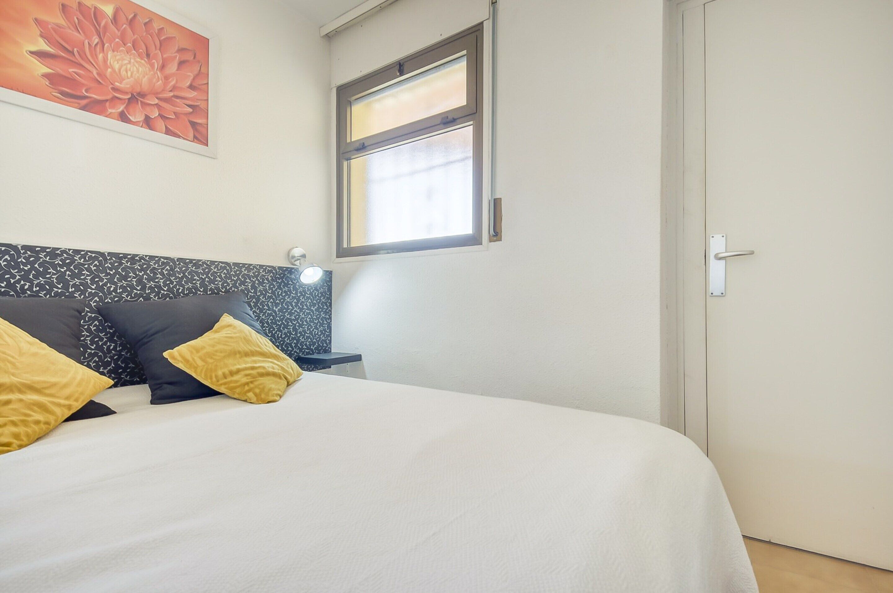 A neatly made bed with a white and black headboard, two yellow pillows, and a wall-mounted nightstand with a lamp.