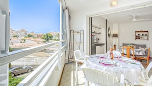 Varanda com vista para a cidade, área de refeições com mesa posta para dois e cozinha visível por uma porta aberta.