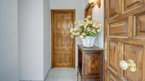 A hallway with a wooden door, a wooden cabinet with a vase of flowers, and a wall-mounted light fixture. - Apartment in Roses Near Cap de Creus (Roses)