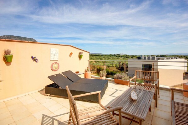 Eine Dachterrasse mit Liegestuhl, zwei Holzstühlen und Topfpflanzen.