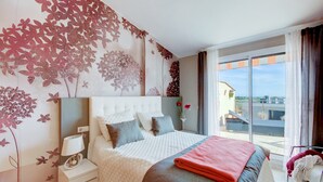 Ein modernes Hotelzimmer mit einem großen Bett, einem Nachttisch, einer Lampe und Blick auf die Stadt durch große Fenster.