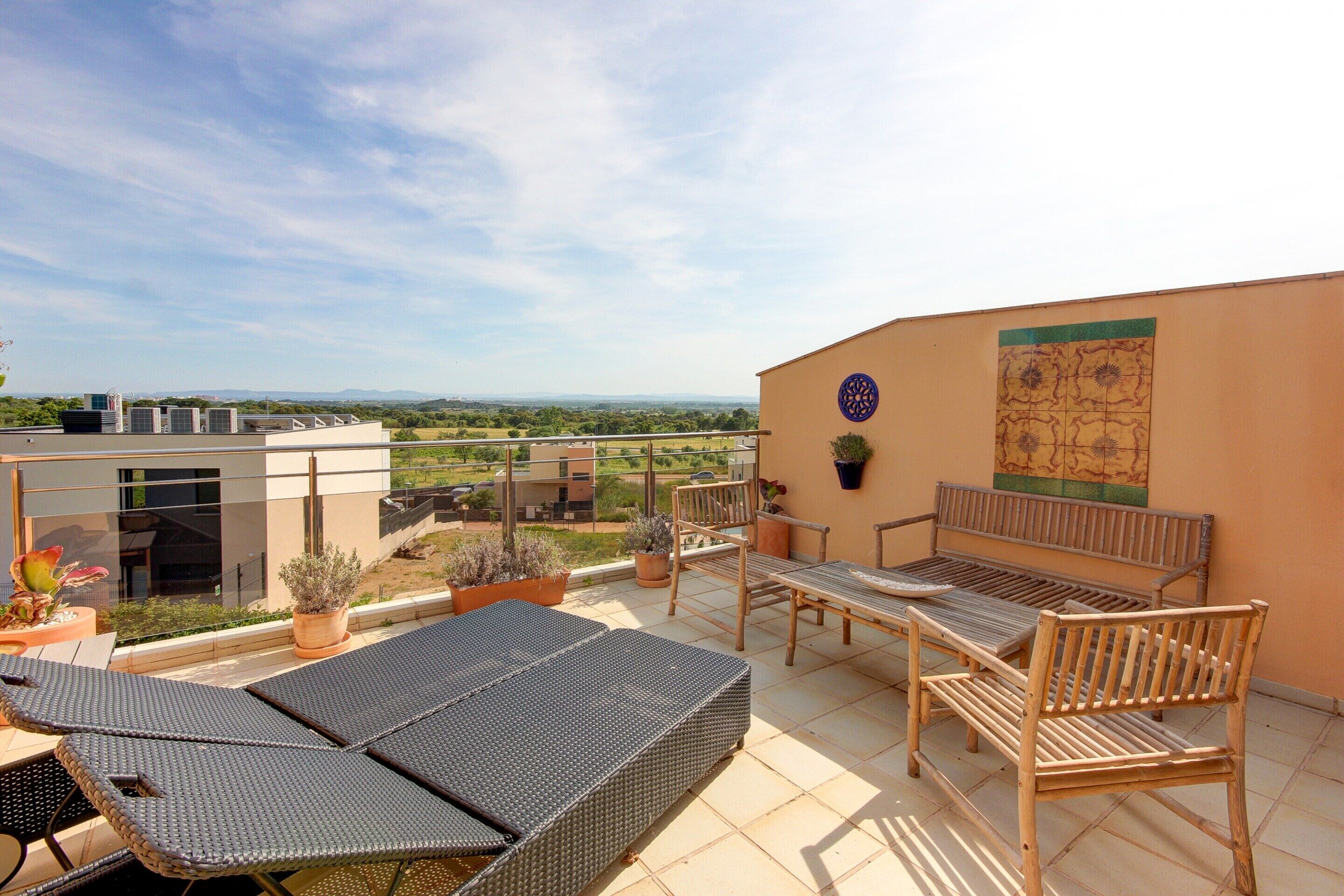 A rooftop terrace with a seating area, potted plants, and a view of the surrounding landscape.