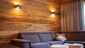 A modern living room with a wooden wall, a sectional sofa, and a round wooden coffee table. - Apartment in Salzburg With Private Balcony (Wagrain)