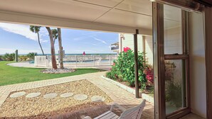 A covered patio with a view of the ocean, a palm tree, and a pathway leading to a beach area. - Directly on the Gulf - Unit  9 - 1 Bedroom - Ground Floor - Sleeps up to 4 (Venice)