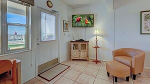 A living room with a television, a wooden cabinet, a chair, and a small table. - Directly on the Gulf - Unit  9 - 1 Bedroom - Ground Floor - Sleeps up to 4 (Venice)