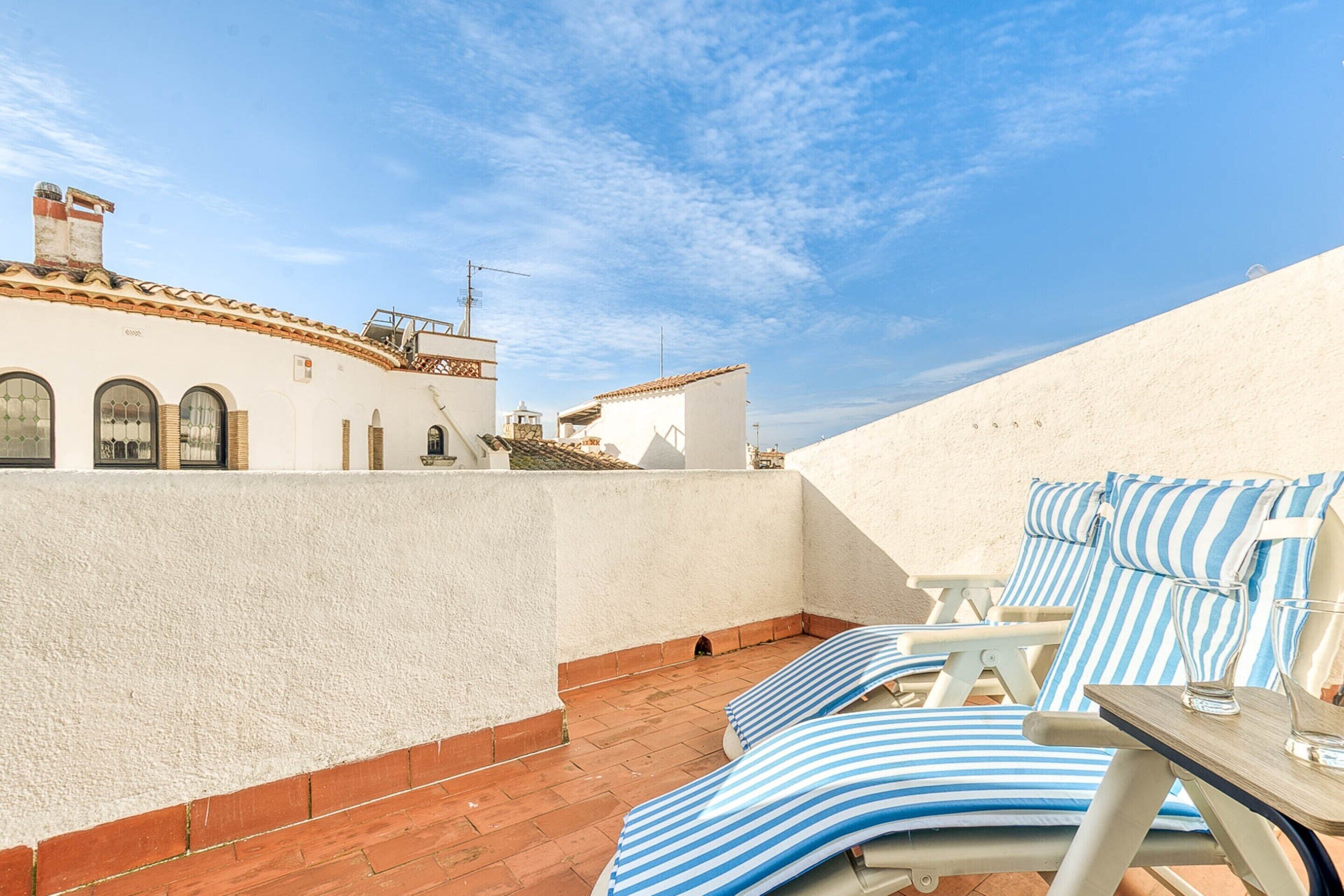 A rooftop terrace with white walls, red-tiled flooring, and blue-striped lounge chairs.