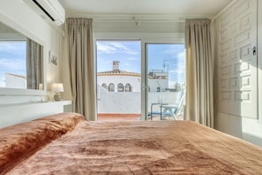 A hotel room with a large bed, a balcony with a view of a building, and curtains on the windows. - Rustic Chic w/ Mooring Spot (Castello d'Empuries)
