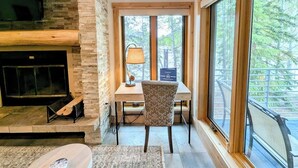A cozy living room with a fireplace, a dining area with a table and chairs, and large windows offering a view of trees. - Private Hot Tub, Views, Summer Adventures (Keystone)