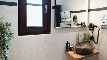 Un baño con tocador de madera, un lavabo redondo, un espejo, un perchero para toallas, un radiador y una ventana.