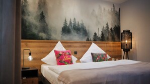 A bedroom with a wooden headboard, a bed with white bedding, two decorative pillows, a nightstand with a lamp, and a wall mural of a forest.