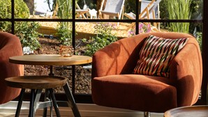 A cozy room with a large window, a wooden table, and a comfortable orange chair with a striped pillow.