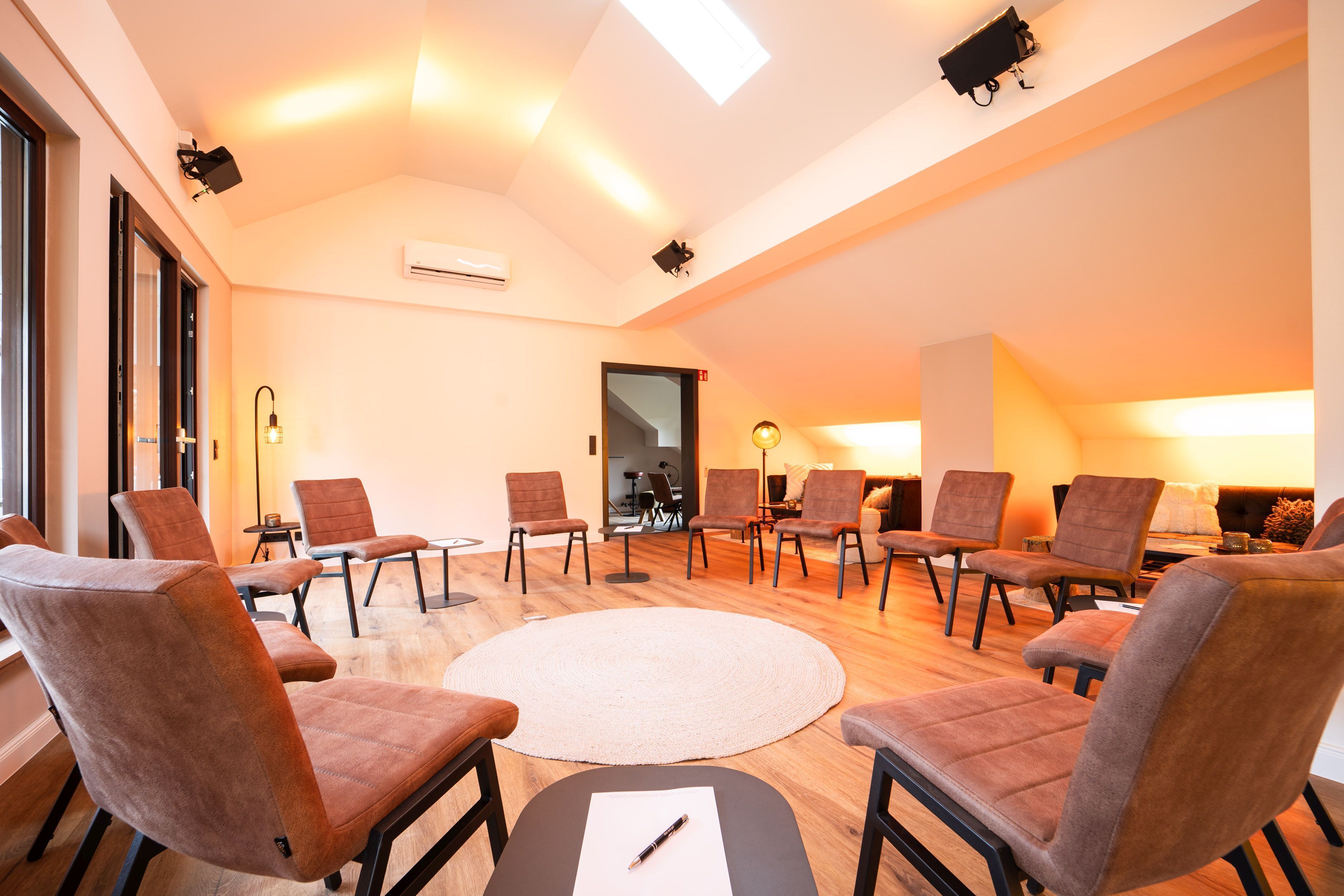 A conference room with a round table, multiple chairs, and a large window.