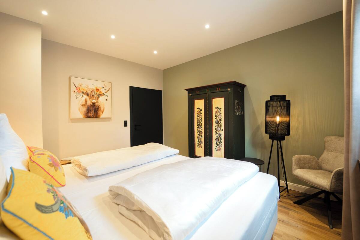 Una habitación de hotel con una cama, una silla, un armario y una lámpara de pie.