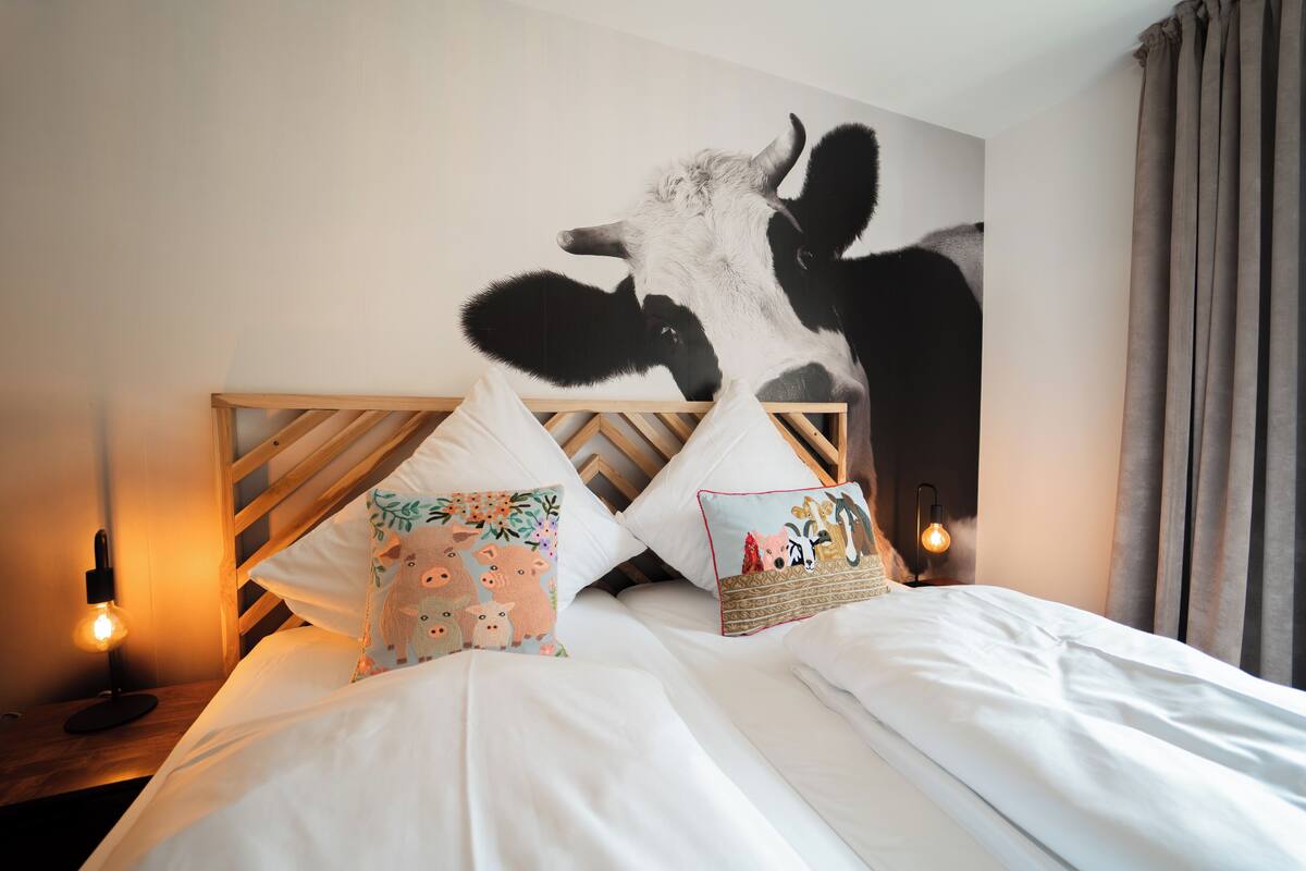 Un dormitorio con un gran mural de una vaca, dos cabeceros de madera y dos lámparas de noche.