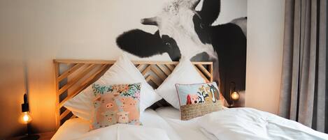 A bedroom with a large wall mural of a cow, two wooden headboards, and two bedside lamps.